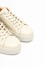 Zapatillas color beige claro, con capellada de cuero suave y acolchado, forro y plantilla de cuero vacuno, y suela de EVA. Tienen una plataforma de 3.8 cm en la parte trasera y 3.2 cm en la delantera.