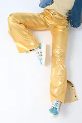 Pantalón de corte flare color verde metalizado, con bolsillos laterales y abertura en los tobillos con botones a presión.
