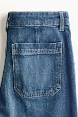 Jean de denim color azul oscuro, con corte wide leg de tiro alto, bolsillos delanteros de parche y pliegues marcados al frente.