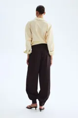 Pantalón de sarga de tiro alto color marrón oscuro, con bolsillos laterales discretos, pinzas y diseño de piernas globo con puños abotonados con frunces.
