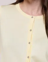 Cardigan de punto fino color amarillo con escote a la base, mangas tres cuartos y abotonadura frontal con botones metálicos decorativos.