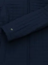 Campera acolchada de estilo quilt marca Tommy Hilfiger, color azul marino, con cuello alto, cierre frontal de cremallera y bolsillos laterales. Presenta un diseño de costuras cuadradas y detalles metálicos en los laterales de la cintura.