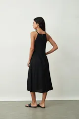 Vestido midi de color negro con escote halter y breteles finos. Presenta un corte holgado y fluido con caída suave.