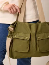 Bolso tipo bandolera de lona color mostaza, con dos bolsillos frontales con solapa y cierre de broche a presión. Cuenta con correas de hombro negras y una correa larga ajustable y extraíble. Presenta herrajes metálicos en tono bronce.