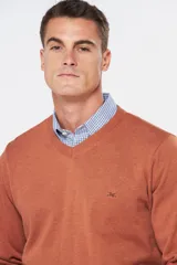 Suéter de tejido fino de algodón, color terracota, con cuello en V y manga larga. Presenta un pequeño logo bordado en el pecho.