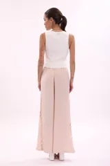 Pantalón largo de tiro alto, color rosa pálido, de corte ancho y fluido. Presenta una hilera de recortes ovalados decorativos a lo largo de la costura lateral.