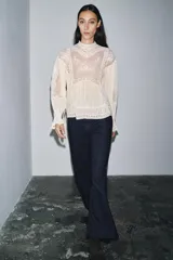 Blusa color crema de algodón con cuello alto, manga larga y bordados florales.