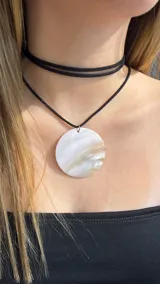 Gargantilla doble de cordón negro con un dije circular grande de nácar natural con vetas tornasoladas.