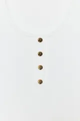 Top de algodón blanco con escote redondo, sin mangas y cierre frontal con pequeños botones. Presenta un diseño acanalado y bajo redondeado.