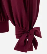 Pantalón de corte aladino con volumen en las piernas, confeccionado en tejido piquet. Presenta cintura elástica y detalle de lazos para anudar en los tobillos.