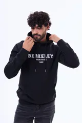 Buzo tipo canguro de felpa color negro, con capucha ajustable mediante cordones, bolsillo frontal tipo canguro y estampa frontal con texto universitario.