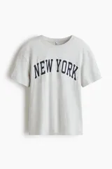 Remera de manga corta, cuello redondo y corte holgado, color gris melange, con estampado arqueado en azul marino que dice "New York".