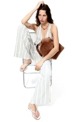 Top halter color beige y azul a rayas, con escote en V pronunciado, tirantes anchos para atar al cuello y detalle de moño ajustable en el centro del pecho. Diseño holgado con leve vuelo en el bajo.