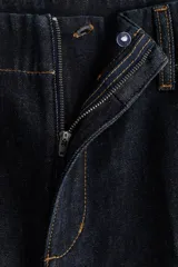 Pantalón de jean estilo wide leg, de tiro alto y corte holgado. Confeccionado en denim rígido de color azul oscuro, presenta costuras a contratono, bolsillos laterales al bies y bolsillos traseros decorativos.