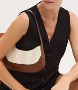 Cartera tipo baguette mediana con cierre de cremallera, correa de mano ajustable y estampado de rayas verticales en tonos beige y blanco. La base de la cartera es de color marrón.