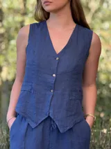 Chaleco azul de lino con corte sastrero, cuello en V, cierre frontal con tres botones de coco y dos bolsillos frontales de parche.