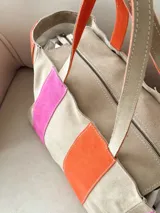 Bolso tipo shopper de diseño amplio, confeccionado en gamuza con un patrón de franjas verticales en tonos marrón oscuro, rosa y verde oliva. Cuenta con doble asa de hombro y cierre superior.