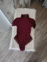 Body de lycra color bordó con cuello alto, mangas cortas y espalda descubierta. Presenta detalles de encaje en el cuello, mangas y laterales de la parte inferior. Cuenta con cierre de broches en la entrepierna.