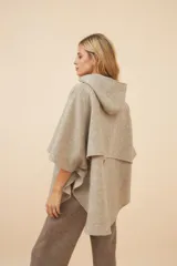 Capa amplia con capucha, confeccionada en lana fina sin teñir. Presenta cierre frontal, bolsillos delanteros y botones laterales que permiten ajustar la forma de las mangas.