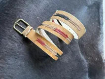 Cinto de cuero marrón claro con detalles bordados geométricos en tonos azul, rojo y beige, hebilla metálica de bronce y puntera forrada en cuero.