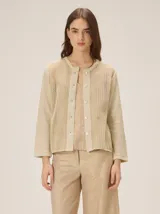 Saco de punto color beige con acabado metalizado, manga larga, cuello redondo y cierre frontal con botones. El diseño combina frente y mangas de tejido abierto con espalda en tela de lino.