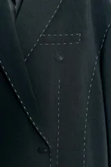 Blazer oversize de corte recto con cuello de solapa, manga larga con hombreras y cierre frontal de doble botonadura. Presenta un diseño en color gris oscuro con costuras decorativas a contraste en color blanco, bolsillos con solapa y forro interior.