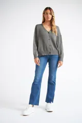 Cárdigan de tejido liviano con textura acanalada, cuello en V y cierre frontal con botones. Presenta mangas largas y un diseño clásico con detalle de grifa en cuero.