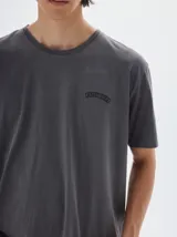 Remera gris oscura de algodón lavado, con cuello redondo, manga corta y corte oversize. Presenta un pequeño logo bordado en el pecho.