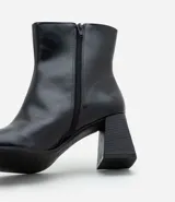 Bota de caña baja en cuero sintético color negro, con punta cuadrada y taco bloque de altura media con textura amaderada.