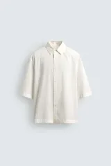 Camisa de corte relajado y boxy fit, confeccionada en tejido con textura irregular. Presenta cuello solapa, manga corta y cierre frontal con botones.