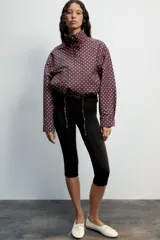 Cazadora negra con estampado de lunares blancos, cuello subido, manga larga, bolsillos delanteros, bajo ajustable con cordones y cierre frontal con cremallera y solapa con botones ocultos.