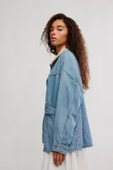 Campera de denim oversize color celeste, con hombro caído, cuello de lona beige en contraste, bolsillos frontales asimétricos, cierre frontal con botones y puños abotonados.