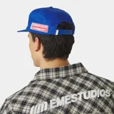 Gorra azul marino con visera curva y cierre ajustable en la parte posterior. Cuenta con un escudo bordado en hilo blanco en la parte frontal con la inscripción "EMESTUDIOS".