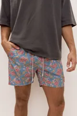 Short de baño celeste con estampa tropical de flores, cintura con cordón ajustable y detalle de etiqueta textil en el lateral.