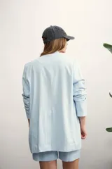 Blazer de mujer color rosa pálido, de corte recto y largo, con solapas de muesca y un solo botón frontal marrón. Presenta bolsillos de parche en la parte delantera y mangas tres cuartos.