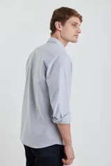 Camisa gris de algodón Oxford, manga larga con puños abotonados y cuello button-down. Tiene un bolsillo de parche en el pecho.