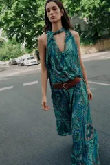 Top sin mangas de cuello alto con lazo ajustable, escote en V y diseño cruzado en el delantero. Presenta un estampado paisley en tonos verdes, azules y rosados, con bajo elástico y forro interior.