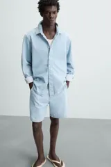 Shorts de denim de algodón, color celeste lavado, de corte regular fit y largo hasta la rodilla. Presenta cierre frontal con cremallera y botón, bolsillos delanteros y bolsillos traseros de plastrón. El borde inferior tiene un acabado deshilachado.