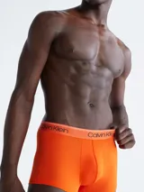 Pack de tres boxers tipo trunk de Calvin Klein, tiro bajo, confeccionados en microfibra elástica que absorbe la humedad. Incluye un boxer naranja, uno blanco/crema y uno beige/tostado, todos con cinturilla elástica con el logo de la marca.