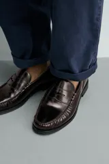 Mocasín de vestir color marrón oscuro, fabricado en cuero, con detalle de antifaz en el empeine y suela a tono con ligero tacón.