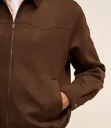 Campera masculina de estilo casual con cuello inglés, cierre frontal por cremallera, bolsillos laterales y ajuste elástico en el bajo. Presenta detalles de recortes en la parte superior delantera.
