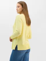 Buzo de tejido fino color amarillo, con cuello redondo, manga larga con puños acanalados y pespunte central vertical en el frente y la espalda. Presenta un ruedo ancho acanalado con tajos laterales.