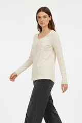 Remera manga larga de algodón color beige, entallada, con cuello redondo y botones en la parte superior. Incluye un bolsillo pequeño en el pecho.