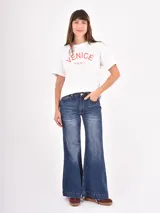 Remera de algodón blanca con cuello redondo y mangas cortas. Presenta un estampado frontal con la palabra 'VENICE' en letras rojas y la frase 'Italy, Amore' en cursiva debajo.