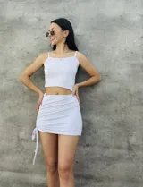 Conjunto blanco de top corto con breteles finos y falda corta con frunce lateral y cordones ajustables.