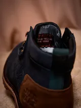 Botines de cuero color azul marino con detalles en cuero marrón en el talón. Presentan un diseño inspirado en Star Wars con el logo grabado en el talón y el Halcón Milenario en el lateral. Cuentan con cordones oscuros, ojales metálicos dorados y una suela robusta de goma en tono tierra.