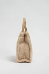 Bolso tipo tote de sherpa color beige con doble asa corta de cuero sintético.