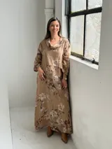 Vestido largo de lino color camel con estampado floral en tonos marrón y crudo, cuello drapeado y mangas largas holgadas.