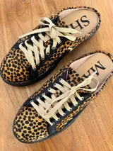 Sueco tipo zapatilla con diseño destalonado, confeccionado en cuero con estampado animal print de leopardo. Presenta cordones en tono beige y suela plana negra.