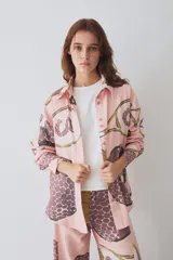 Camisa de corte recto y manga larga con cuello clásico y cierre frontal de botones. Presenta un estampado artístico de temática deportiva en tonos rosados, marrones y ocres, con un bolsillo frontal aplicado.